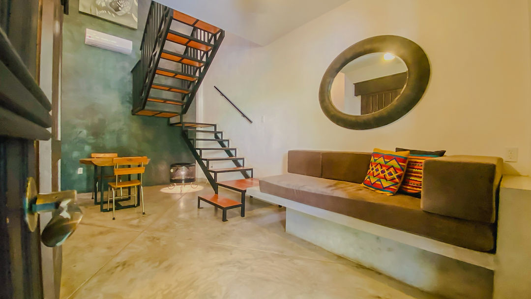 Interior de loft con escalera, sala y espejo redondo